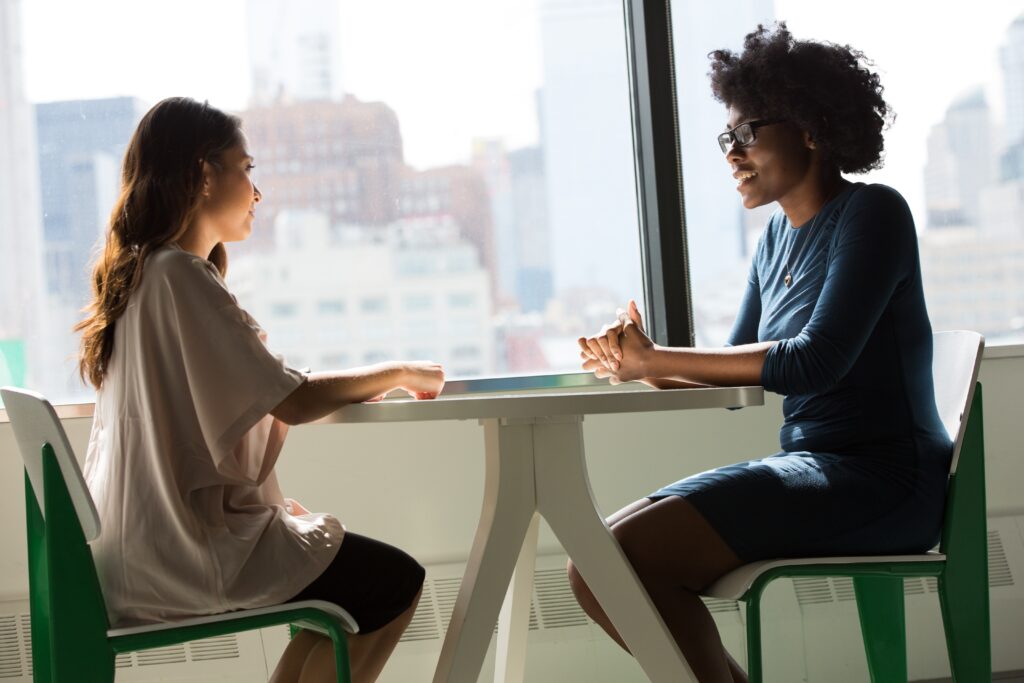 two people sitting at a table talking in front of a window